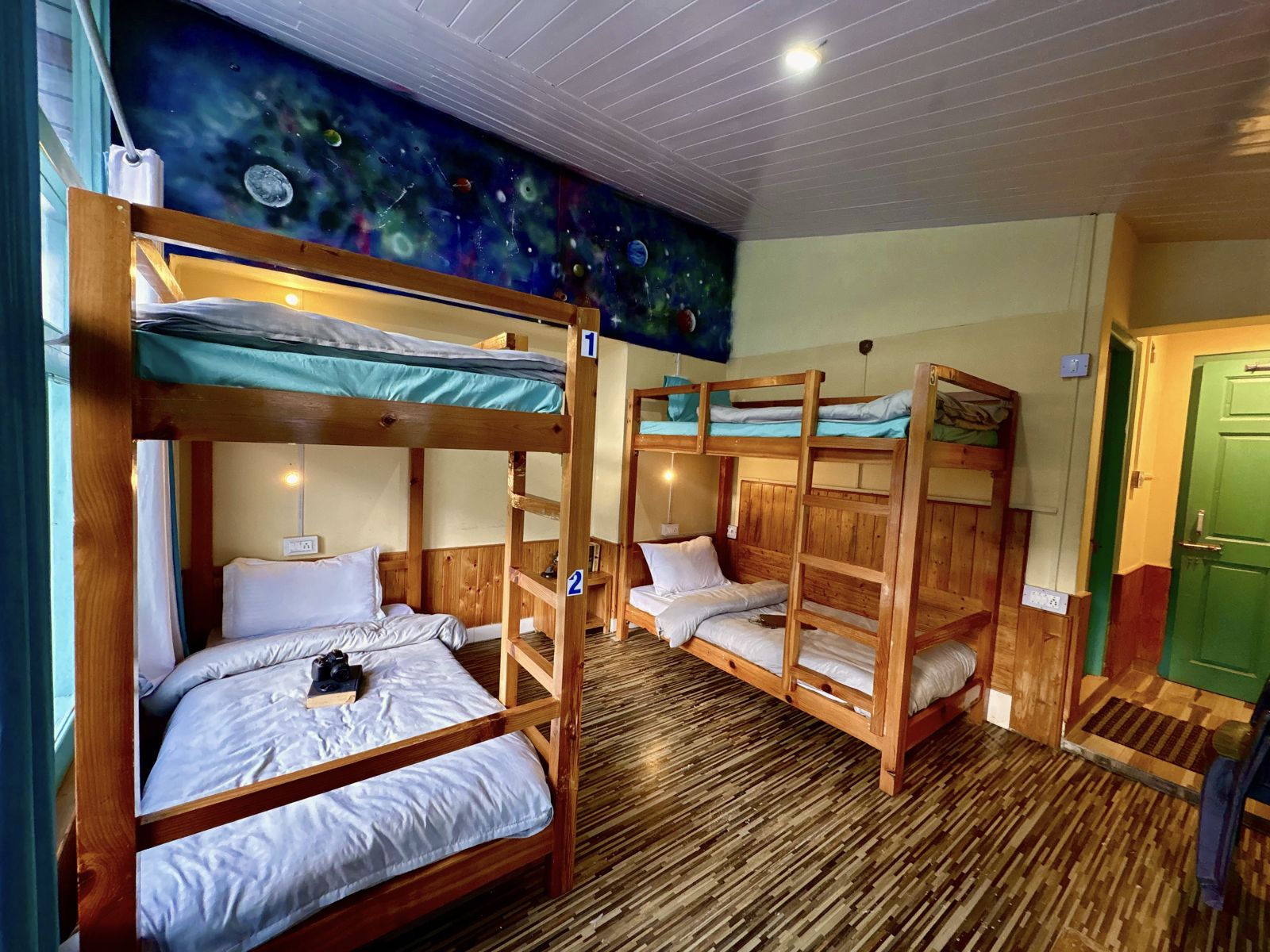 Four-bed dorm with wooden bunk beds and a space mural at Misfits